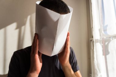 Tüm yüzünü kaplayan beyaz kağıt maskeli genç Latin bir adam. Boş çarşaf, gölge. O, elleriyle kostümü çıkarıyor. Bogota, Kolombiya 'da güneşli bir gün.