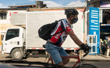 Bogota, Kolombiya 'da Rojas caddesinde bisiklete binen Latin erkek bisikletçi. Corona virüsünün yayılmasını önlemek için maske takıyor. Miğfer, şort ve sırt çantası. Kamyon arkada.. 
