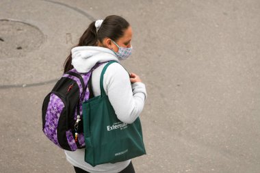 Kolombiya, Bogota sokaklarında yürürken maske takan genç bir kadın. Koronavirüs kapmaktan ve yayılmaktan kaçının. Kazak. Externado Üniversitesi 'nden yeşil çanta.. 