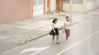 İki kadın, genç ve orta yaşlı, biri maske takıyor, Bogota, Kolombiya sokaklarında yürüyor. Koronavirüs kapmaktan ve yayılmaktan kaçının. Gayri resmi kıyafetler.