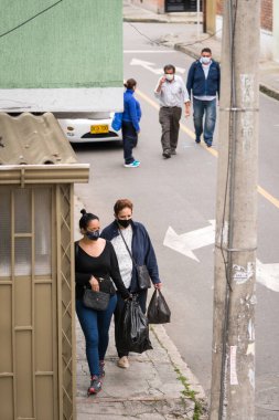Maske takan yaşlı ve orta yaşlı kadınlar ve erkekler Bogota, Kolombiya sokaklarında yürüyorlar. Siyah plastik torbalar taşıyordu. Koronavirüsü kapmaktan ve yaymaktan kaçının.. 