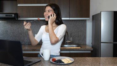 Genç bir kadın kahvaltı yaparken telefonda konuşuyor.