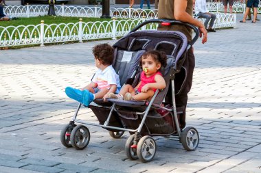 Istanbul, Türkiye - 21 Ağustos 2018: İkizler, küçük erkek ve kız bebek arabası içinde sıcak güneşli bir kare Sultanahmet'te oturuyorsun