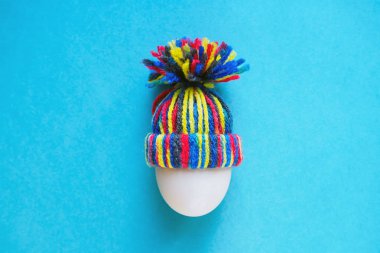 mavi arka plan, Paskalya kavramı üzerinde renkli örgü yün şapkalı beyaz yumurta