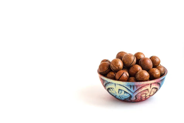 Clay bowl with macadamia nuts in shell on white background, copy space — Stock Photo, Image