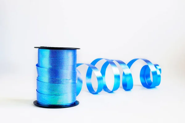 Spool of blue curling ribbon roll for gift wrapping art and crafts on white background. Selective focus, copy space