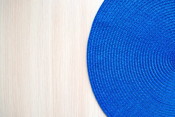 Blaue runde gewebte Textilmatte auf beigem Holzhintergrund. Kopierraum, Ansicht von oben — Stockfoto