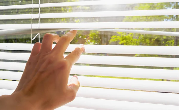 Mão abre-se com cortinas de dedos, fora da janela há luz solar e árvores verdes. Conceito verão quente e sol escaldante — Fotografia de Stock