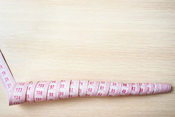 Top view of curly measuring tape on a beige wooden background, copy space — Stock Photo, Image