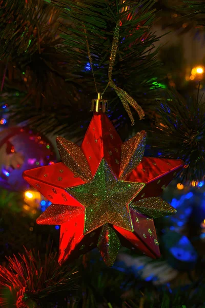Red toy in the form of a star hangs on a christmas tree with garlands Royalty Free Stock Photos