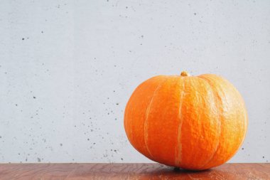 Kahverengi ahşap masada turuncu balkabağı ve gri beton duvara karşı. Boşluğu kopyala.