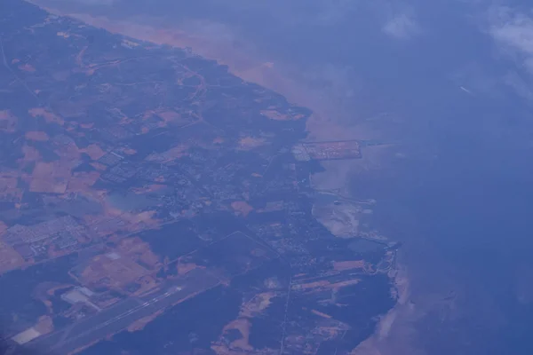 View from an airplane out of the window flying above the ocean with blue sky and clouds. Bird eyes view of the planet.