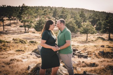 Mutlu ve genç hamile çift doğada sarılıyorlar.