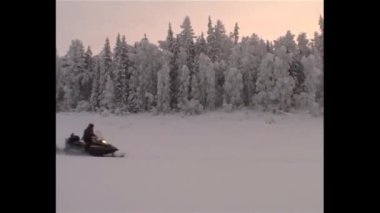 Kış, nehrin buzu üzerinde silahlı bir kar aracı avcısına gider ve onu av köpeği izler..