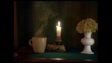 Masanın üzerinde yanan bir mum ve bir fincan sıcak çay var..