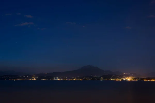 Peschiera del Garda sahilinden Garda Gölü 'ne ve diğer kıyılarda ışıkları olan dağlara gece çekimleri. Garda 'nın ışıkları gecenin karanlığında diğer kıyıdan.