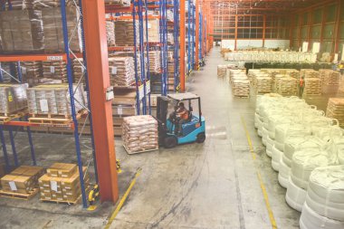 Büyük bir dağıtım deposunda yük paletleri düzenleyen forklift manzarası. Depo lojistik operasyonları. Depo işçisi ve forklift sürücüsü.
