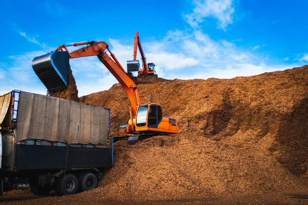 Büyük odun parçalarının üzerinde duran kepçe kamyona yükleniyor. Woodchips hammadde depolama ve taşımacılığı.