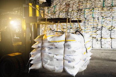 Forklift, ambarın içindeki yığına koymak için rafine beyaz şeker dolu bir çanta taşıyor. Şeker deposu işlemleri ve yönetimi.