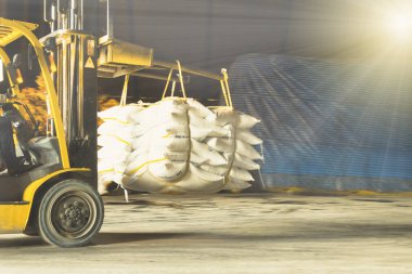 Forklift, ambarın içindeki yığına koymak için rafine beyaz şeker dolu bir çanta taşıyor. Şeker deposu işlemleri ve yönetimi.