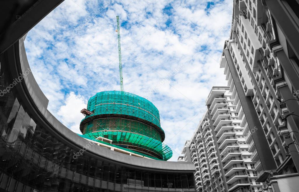 Urban architecture, circular structure building under construction with cloudy sky. Selective color.