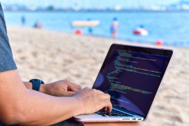 Güneşli bir yaz gününde kumsalda kaynak kodları yazan bir programcı. Öğrenim, Çalışma, Teknoloji, Serbest Çalışma Konsepti.
