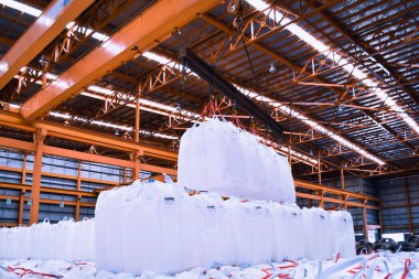 Overhead crane lift jumbo bags of tapioca using spread bar in storage warehouse. Bulk cargo in jumbo bag handling equipment.  clipart