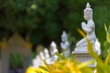 Yeşil bahçe arka planında el çırpılmış birden fazla beyaz Budist heykeli.
