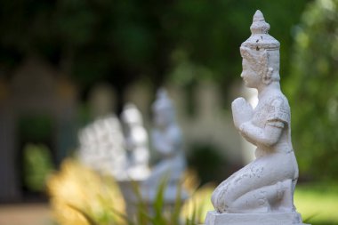 Yeşil bahçe arka planında el çırpılmış birden fazla beyaz Budist heykeli.