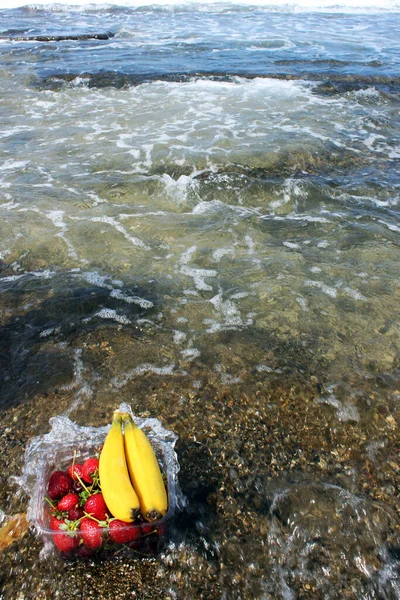 Muz ve çilek bir sepetin içinde, denizin kenarında yatıyor.
