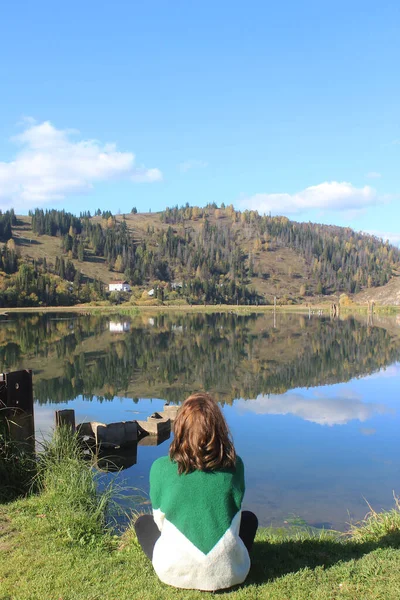 Sonbaharda yeşil kazaklı genç bir kadın gölün kenarında oturur.