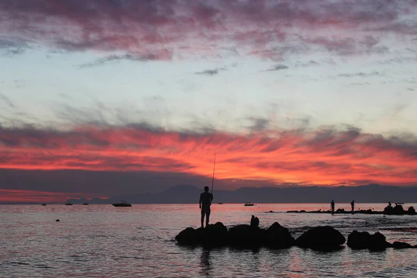 Adam gün batımında denizde balık tutuyor. Siluet.