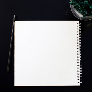 Model yap. Siyah arka planda beyaz defter. Aksesuarlar ve çiçeklerle dolu bir ofis masası. Kopyalama alanı olan üst görünüm.