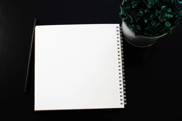 Model yap. Siyah arka planda beyaz defter. Aksesuarlar ve çiçeklerle dolu bir ofis masası. Kopyalama alanı olan üst görünüm.