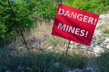 Red sign DANGER MINES in front of a minefield fenced with barbed wire clipart