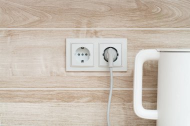 Beyaz elektrikli su ısıtıcısı elektrik prizine takılmış. Duvara takılmış, mutfağa takılmış.