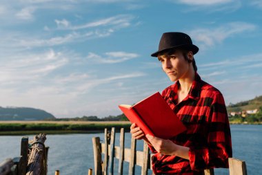 Şapkalı güzel bir kadın eski bir nehir iskelesinde kitap okuyor. Boş zaman ve boş zaman kavramı. yaz zamanı.