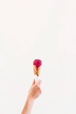 Açık kahverengi arka planda ahududulu dondurma külahı. Dondurmayı elle tutan kadın. yaz konsepti