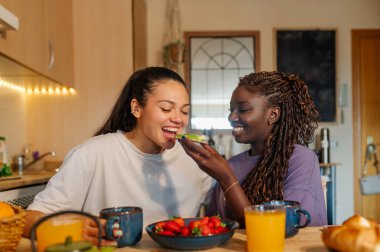 Mutfaklarında canlı, sağlıklı bir kahvaltı yapan iki kadın lezzetli yiyecekler, kahkahalar ve sıcak bir atmosferde sıcak bir gülümseme paylaşıyorlar.