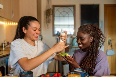 İki kadın, sıcak mutfaklarında keyifli bir kahvaltı yaparken tostlarına vegan sosu ekliyor.