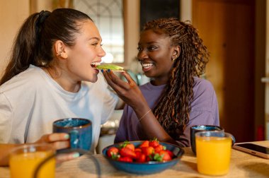 Evde sağlıklı bir kahvaltı yapan iki kadın avokado tostu, çilek ve portakal suyu yiyor.