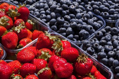 Çok sayıda kırmızı olgun çilek ve organik yaban mersini küçük plastik kaplarda satılıyor.
