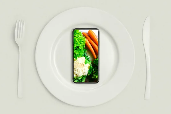 Consegna di cibo per l'acquisto a domicilio via Internet. Chiamali e porteranno il cibo a casa. Smartphone con verdure fresche in un negozio online sullo schermo, sdraiato su un piatto, coltello e forchetta. La vista da — Foto Stock