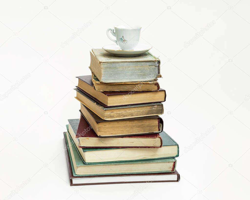 a stack of old books. Upstairs is an elegant coffee cup and saucer. On white background.