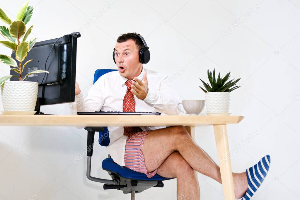The male manager works remotely at home, holds an online meeting. He experiences an emotion of discontent and indignation. He is wearing a shirt and tie, underpants and slippers. Stay home and