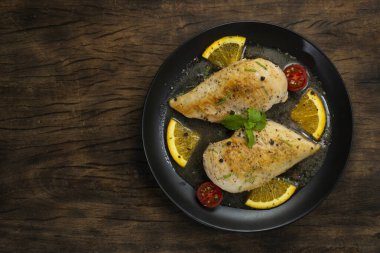 Portakal ve tereyağlı tavuklu Piccata siyah tabağa iyi gelir İtalyan Gıda Füzyon Tarzı En Popüler Sebze ve Domates Üst Görünümü dekore eder