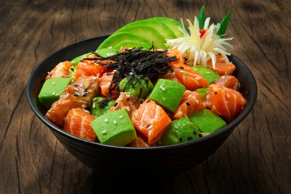Salmon Poke Bowl with Avocado ingredients Ahi shoyu,Vinegar, sesame, onion Healthy Food Hawaii Poke don style combination Japanese food famous popular meal on wood background decorate with leek flower shape sideview