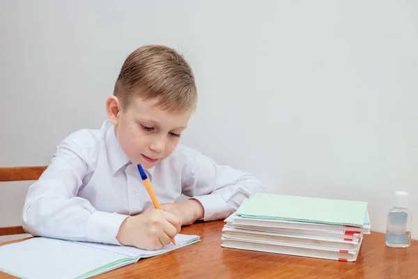 A fiú az asztalnál ül, tollat tart, jegyzetfüzetek és tankönyvek mellett. — Stock Fotó