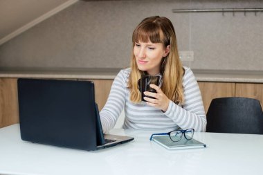 Avrupa görünümlü bir kız masada oturuyor ve dizüstü bilgisayara bakıyor.