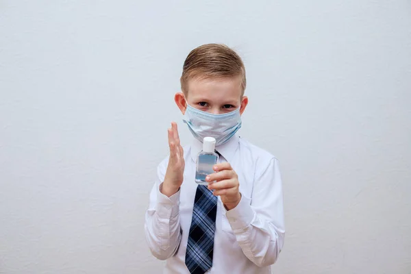 Um menino mascarado com uma camisa branca e gravata está segurando um desinfetante de álcool — Fotografia de Stock
